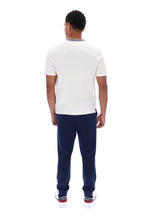 A man viewed from behind wearing a white short-sleeve crewneck t-shirt with a gray collar trim, navy blue pants, and white sneakers with red accents, shot against a solid white background.