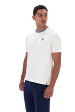 A man wearing a white short-sleeve ringer t-shirt with a gray crew neck and a small red, white, and blue Fila logo on the left chest, paired with navy blue pants, against a plain white background.