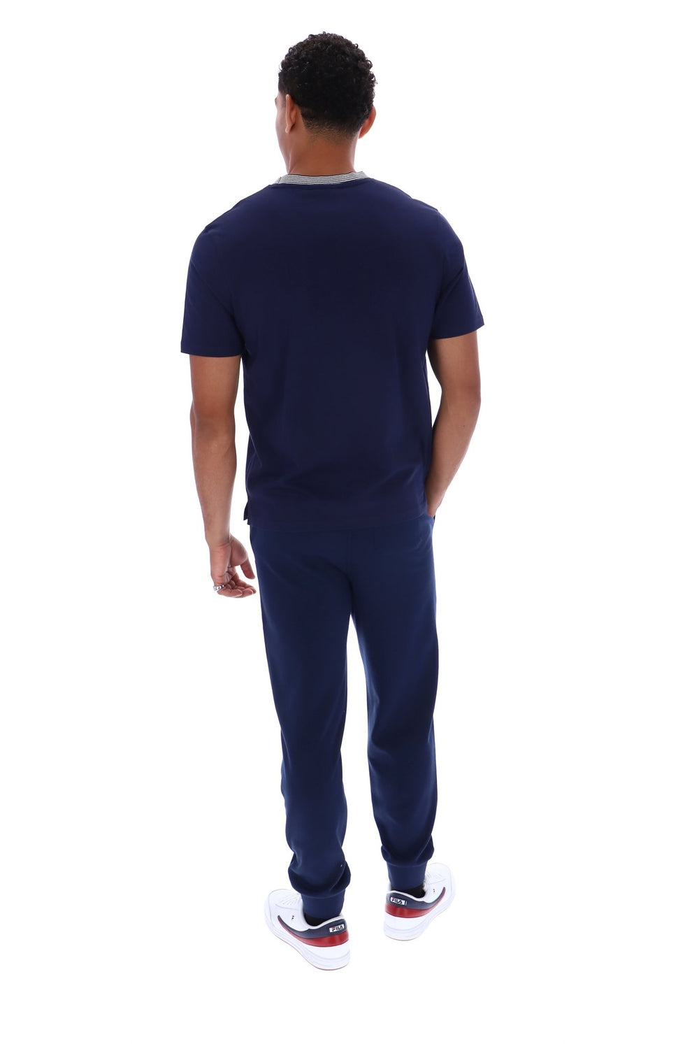 A man viewed from behind wearing a navy blue short-sleeve t-shirt and matching navy blue sweatpants, paired with white sneakers, against a solid white background.