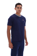 A man wearing a navy blue short-sleeve t-shirt with a gray crew neck collar and a small red and white logo on the left chest, paired with matching navy pants, against a plain white background.