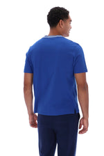 A man viewed from the back wearing a royal blue short-sleeve crewneck t-shirt and navy blue pants, set against a plain white background.