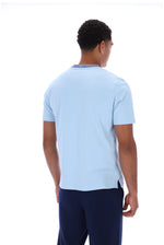 A man viewed from behind wearing a light blue short-sleeve crewneck t-shirt and navy blue pants, photographed against a solid white background.