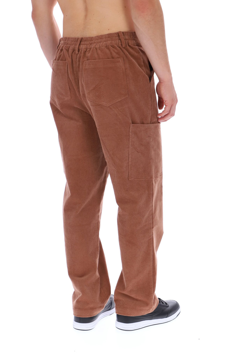 A man shown from the back wearing brown corduroy pants with an elastic waistband, side pockets, and cargo-style pockets on the legs, paired with black and white sneakers against a white background.