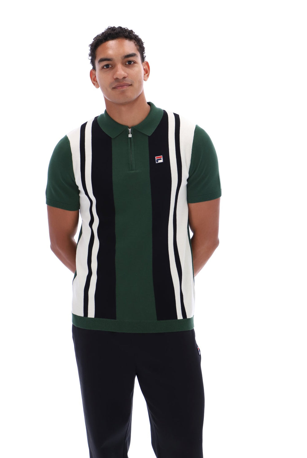 A man wearing a green, black, and white striped knit polo vest with a small red and white Fila logo on the chest, paired with black pants, against a plain white background.