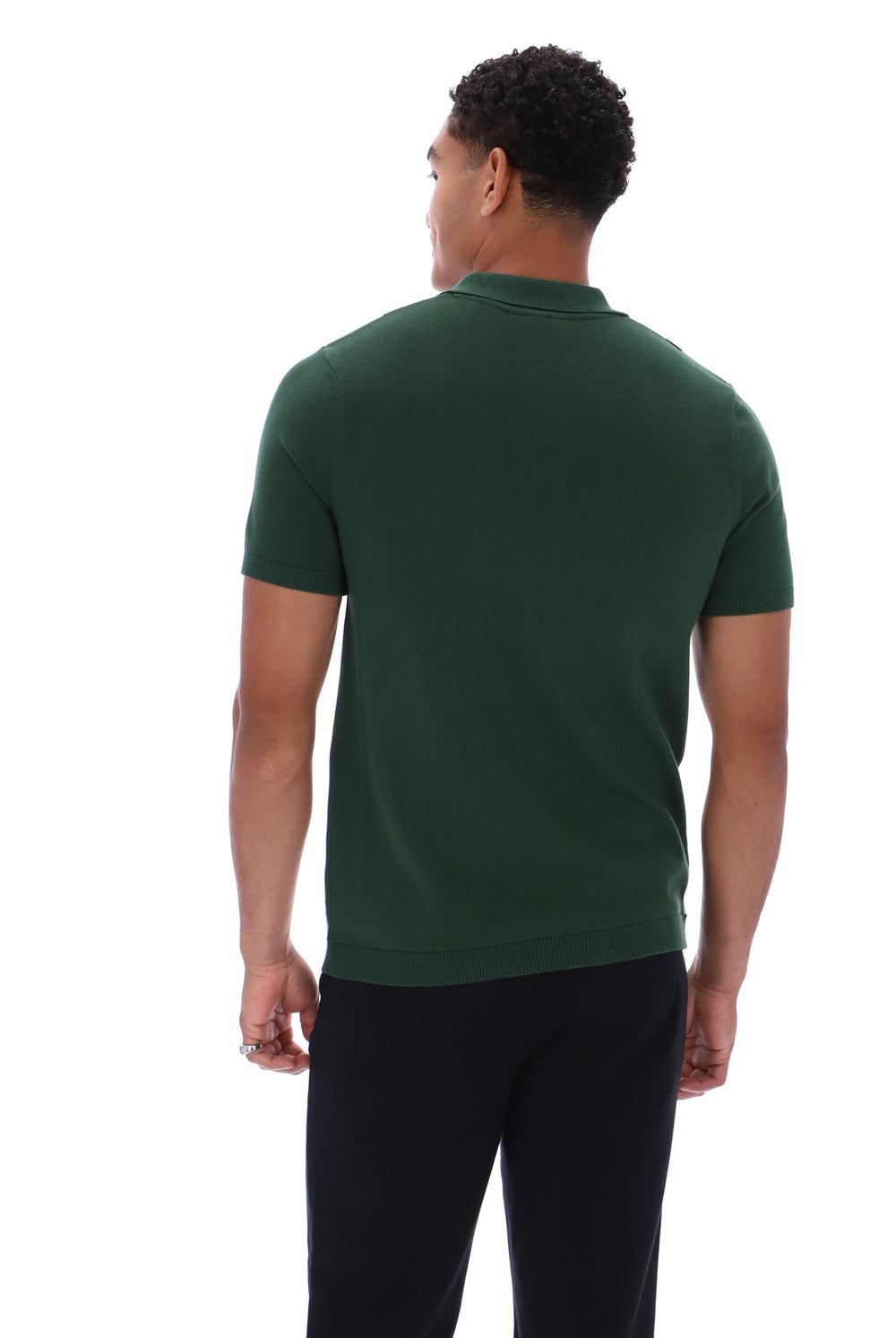 A man viewed from the back wearing a dark green short-sleeve polo shirt and black pants, photographed against a plain white studio background.