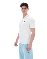Man wearing a white polo shirt and light blue pants on a white background