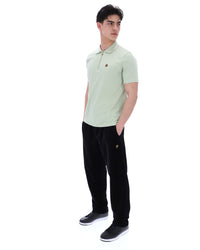 Man wearing a light green polo shirt and black pants on a white background