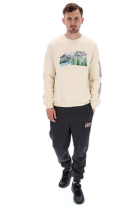 A male model wearing a beige FILA Len Graphic Crew Sweatshirt with a mountain range and brand logo on the front.