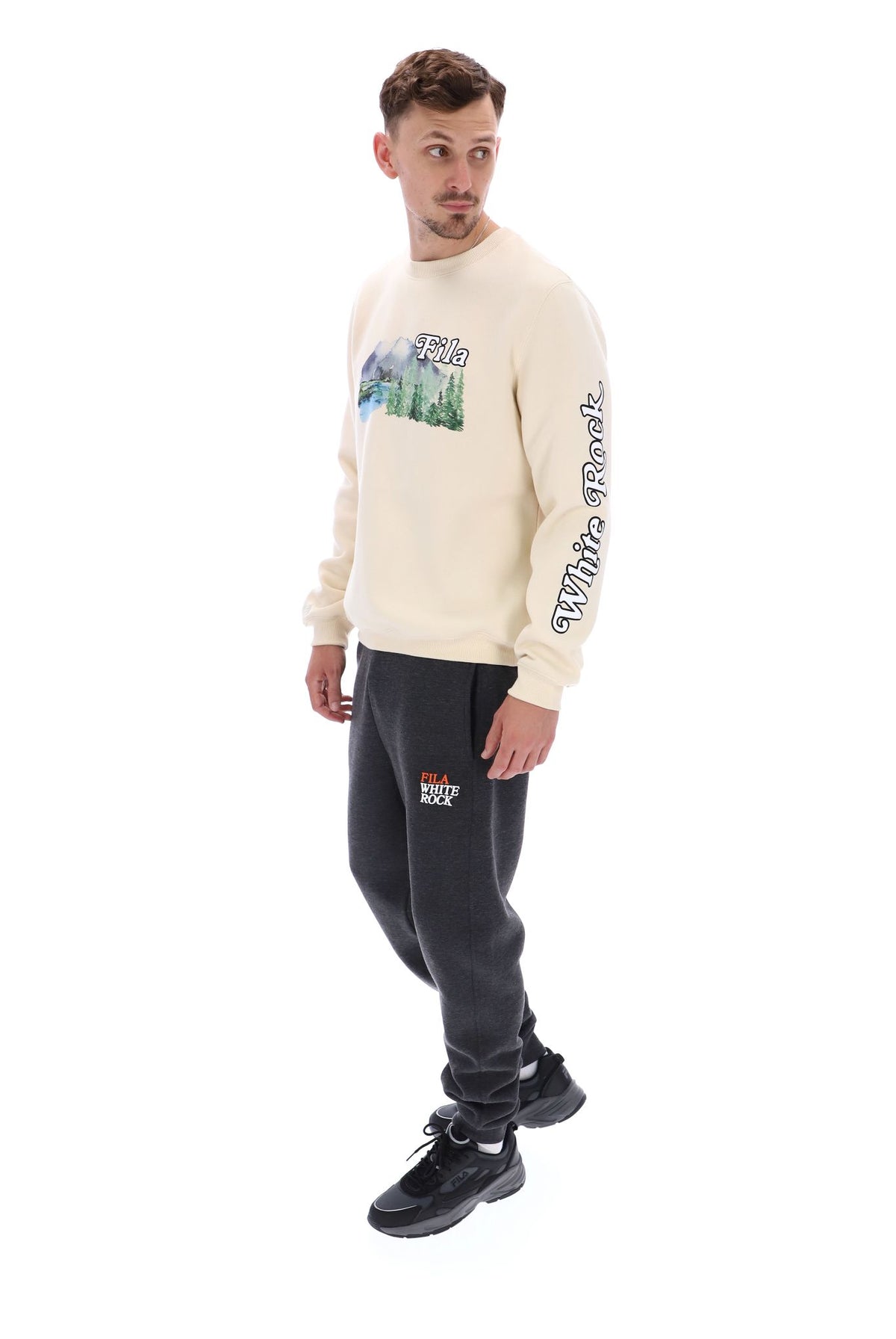 A male model wearing a beige FILA Len Graphic Crew Sweatshirt with a mountain range and brand logo on the front.