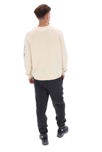 A male model wearing a beige FILA Sweatshirt with black trousers and bottoms.