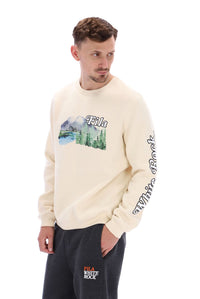 A male model wearing a beige FILA Len Graphic Crew Sweatshirt with a mountain range and brand logo on the front.
