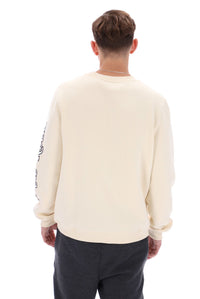 A male model wearing a beige FILA Sweatshirt with black trousers and bottoms.
