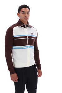 A man wearing a brown, white, and light blue striped quarter-zip track jacket, paired with black pants, photographed against a solid white background.