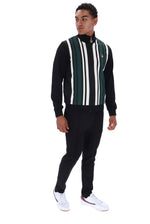 A man modeling a black knit zip-up sweater vest with vertical green, white, and black stripes on the front, paired with black joggers and white sneakers, against a plain white background.