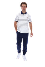 A man modeling a white short-sleeve polo shirt with navy blue horizontal stripes, a navy collar, and a small embroidered logo on the chest, paired with navy jogger pants and white sneakers, against a plain white background.