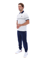 A man modeling a white short-sleeve polo shirt with navy blue horizontal stripes, navy collar and sleeve trim, navy jogger pants, and white sneakers, shown against a plain white background.