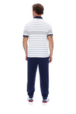 A man viewed from behind wearing a white short-sleeve polo shirt with thin navy horizontal stripes and navy trim, paired with navy jogger pants and white sneakers.