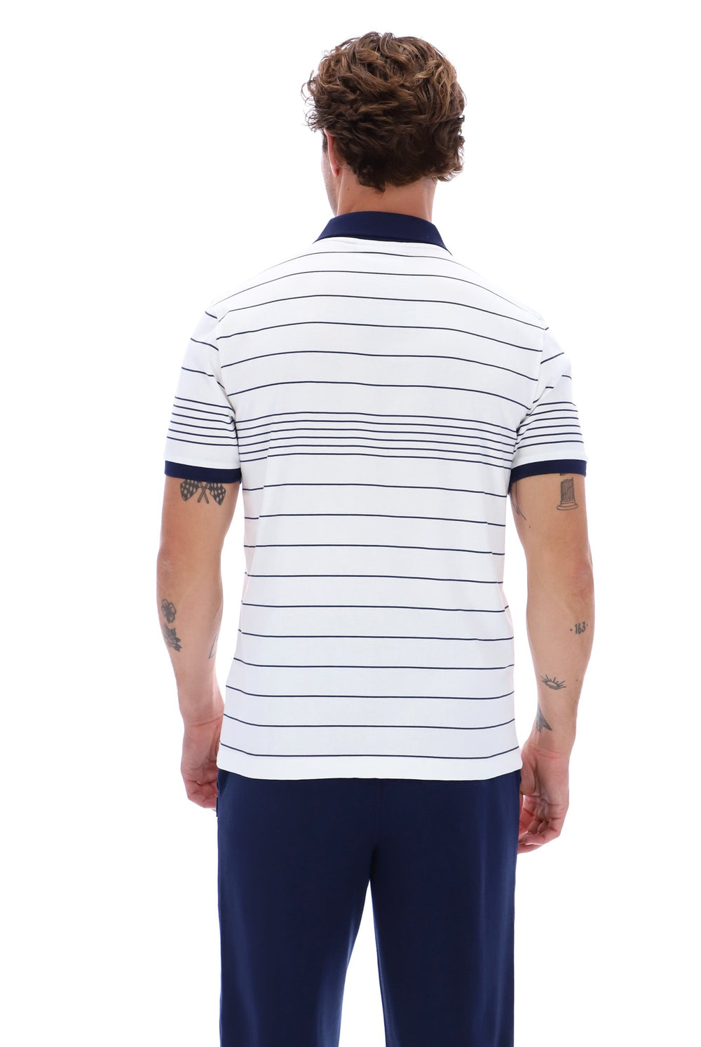 A man viewed from the back wearing a white short-sleeve polo shirt with thin navy horizontal stripes and a navy collar, paired with navy pants, against a plain white studio background.