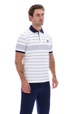 A man wearing a white short-sleeve polo shirt with thin navy blue horizontal stripes, a navy collar, and a small red and white embroidered logo on the chest, paired with navy pants, against a plain white background.