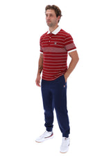 A man modeling a red and white striped polo shirt with navy blue jogger pants and white sneakers, featuring the Fila logo on the chest and thigh.