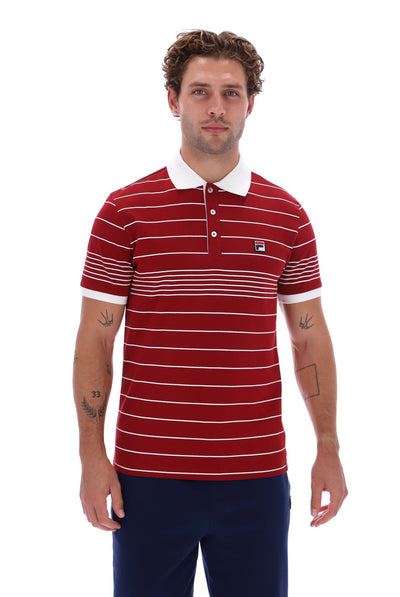 A man wearing a red and white horizontally striped short-sleeve polo shirt with a white collar and navy blue pants, standing against a plain white background.