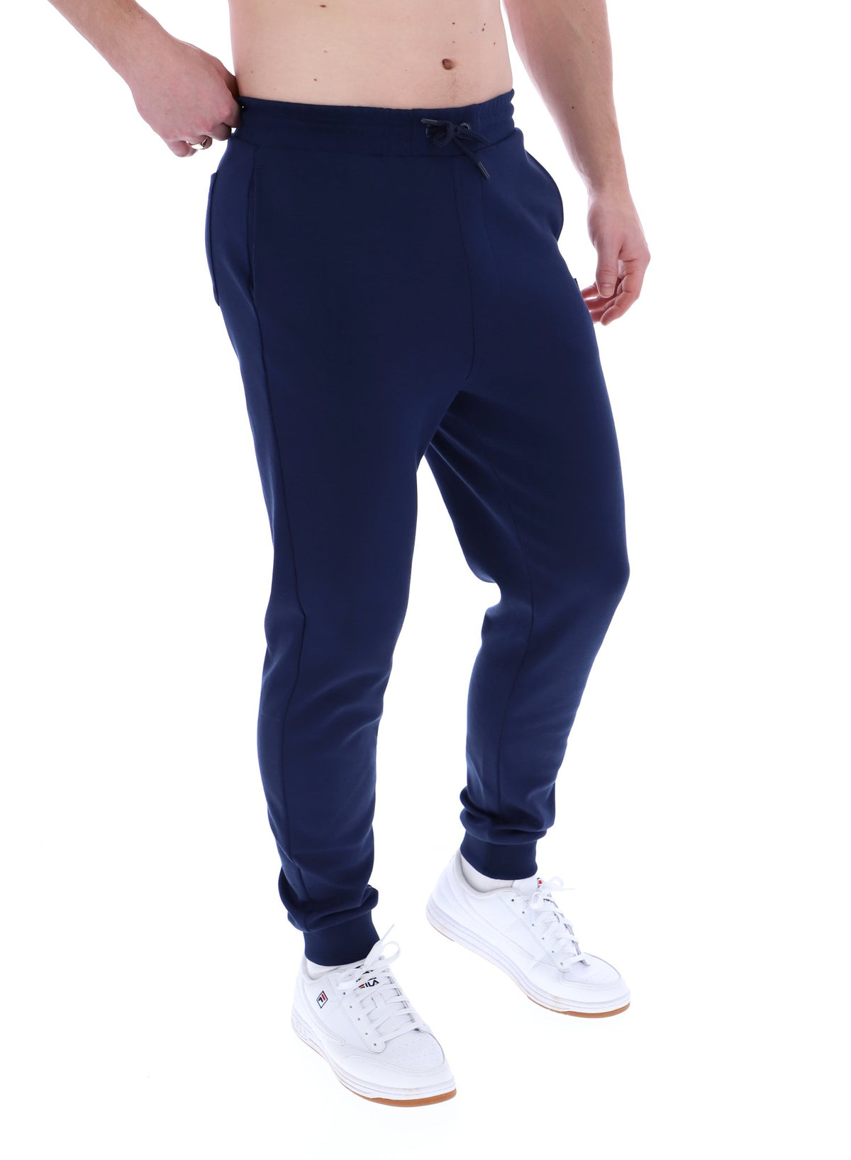 A person standing and wearing navy blue Lonny drawstring joggers with a drawstring waistband and cuffed design, featuring FILA logo branded on the waistband.
