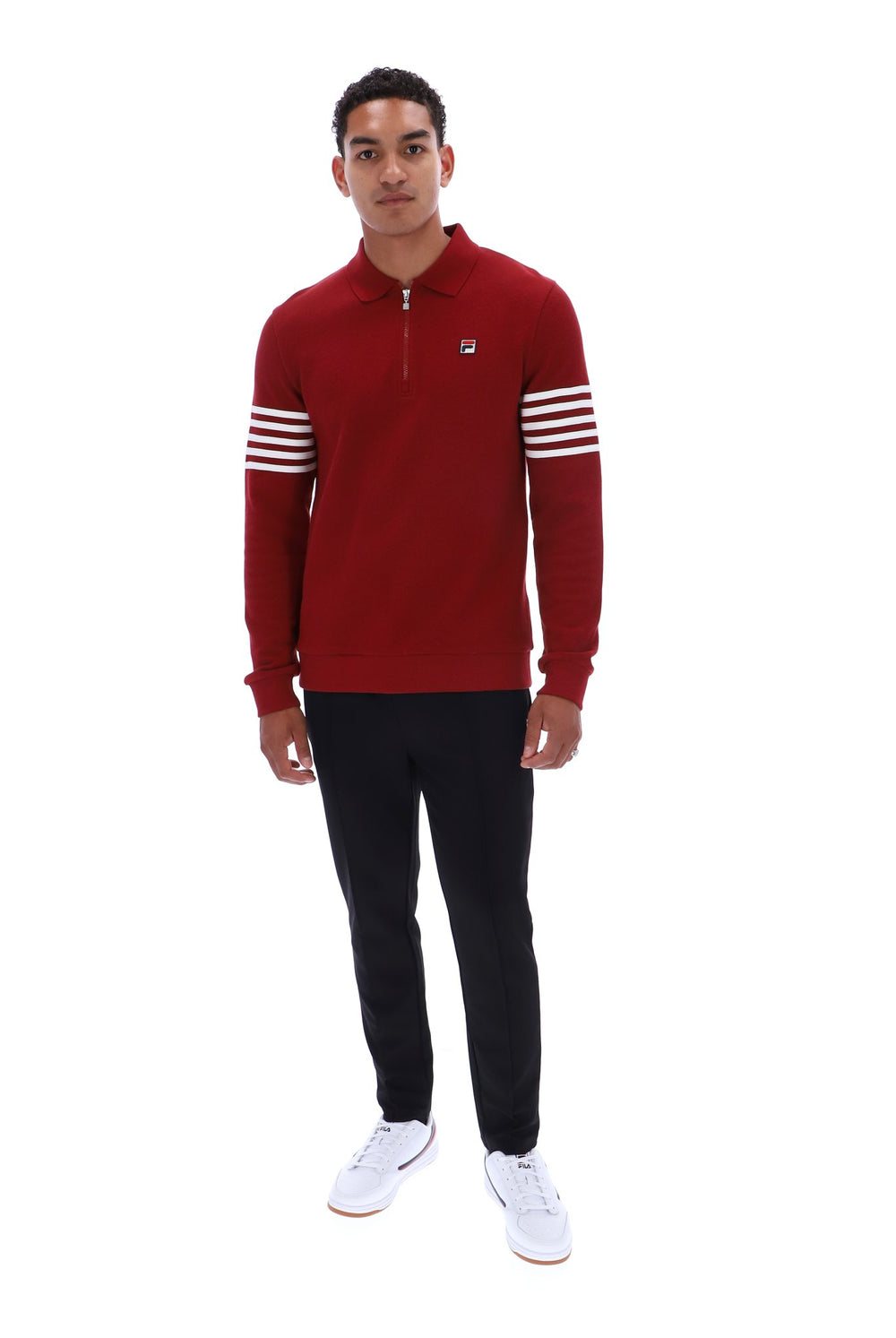 A man modeling a red long-sleeve quarter-zip pullover with white stripes on the sleeves, paired with black pants and white sneakers, against a plain white background.