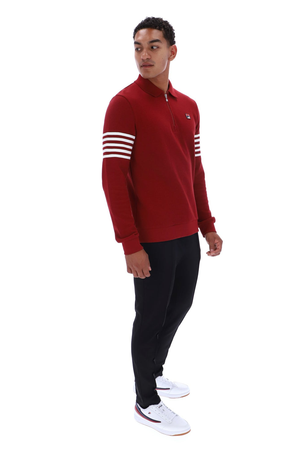 A man modeling a red long-sleeve quarter-zip pullover sweatshirt with white stripes on the sleeves, paired with black pants and white sneakers, against a plain white background.