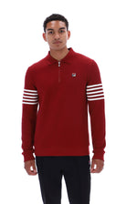 A man wearing a red long-sleeve quarter-zip pullover sweatshirt with white stripes on the sleeves and a small Fila logo on the chest, paired with black pants, against a plain white background.