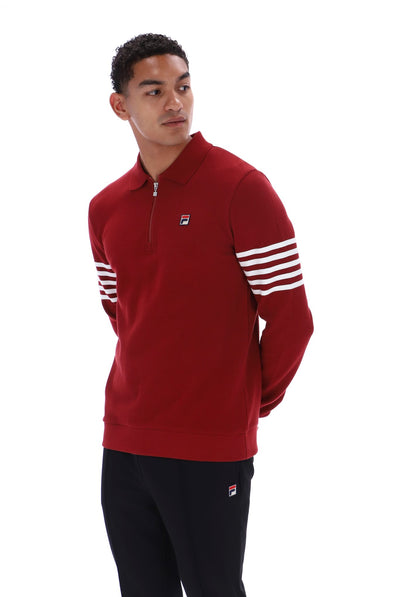 A man wearing a red half-zip pullover sweatshirt with white stripes on the sleeves and black pants, photographed against a plain white background.