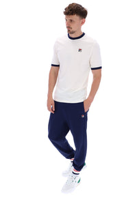 A male model wearing a white and navy ringer t-shirt with the FILA logo on the chest, paired with navy FILA joggers, on a white background