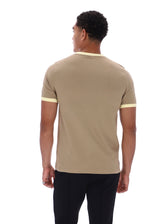 A man viewed from the back wearing a beige short-sleeve t-shirt with light yellow contrast trim at the collar and sleeve cuffs, paired with black pants, against a plain white background.