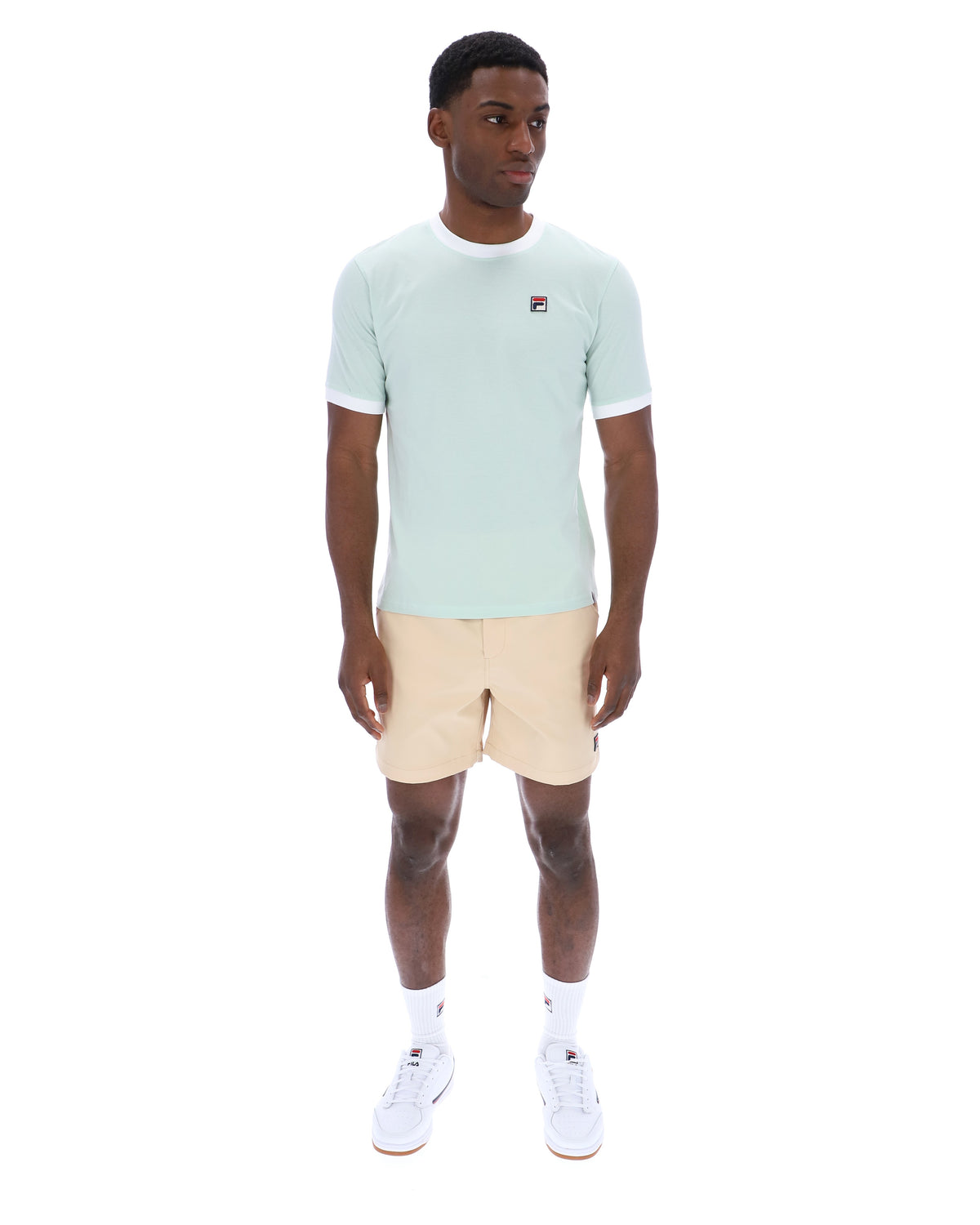 Man wearing a light green t-shirt and beige shorts on a white background