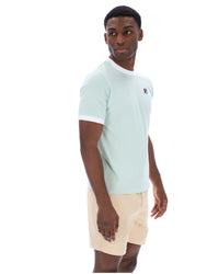 Man wearing a light green polo shirt and beige shorts on a white background
