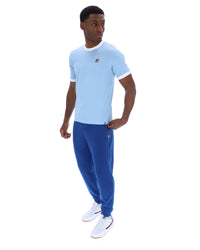 Man wearing a light blue t-shirt and blue pants with a visible brand logo on a white background