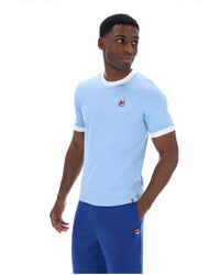 Man wearing a light blue t-shirt and blue pants with a brand logo on a white background