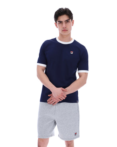 Man wearing a navy t-shirt with a FILA logo and grey shorts with a FILA logo on a white background