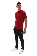 A man modeling a red short-sleeve t-shirt with black trim and black joggers, paired with white sneakers, against a plain white background.