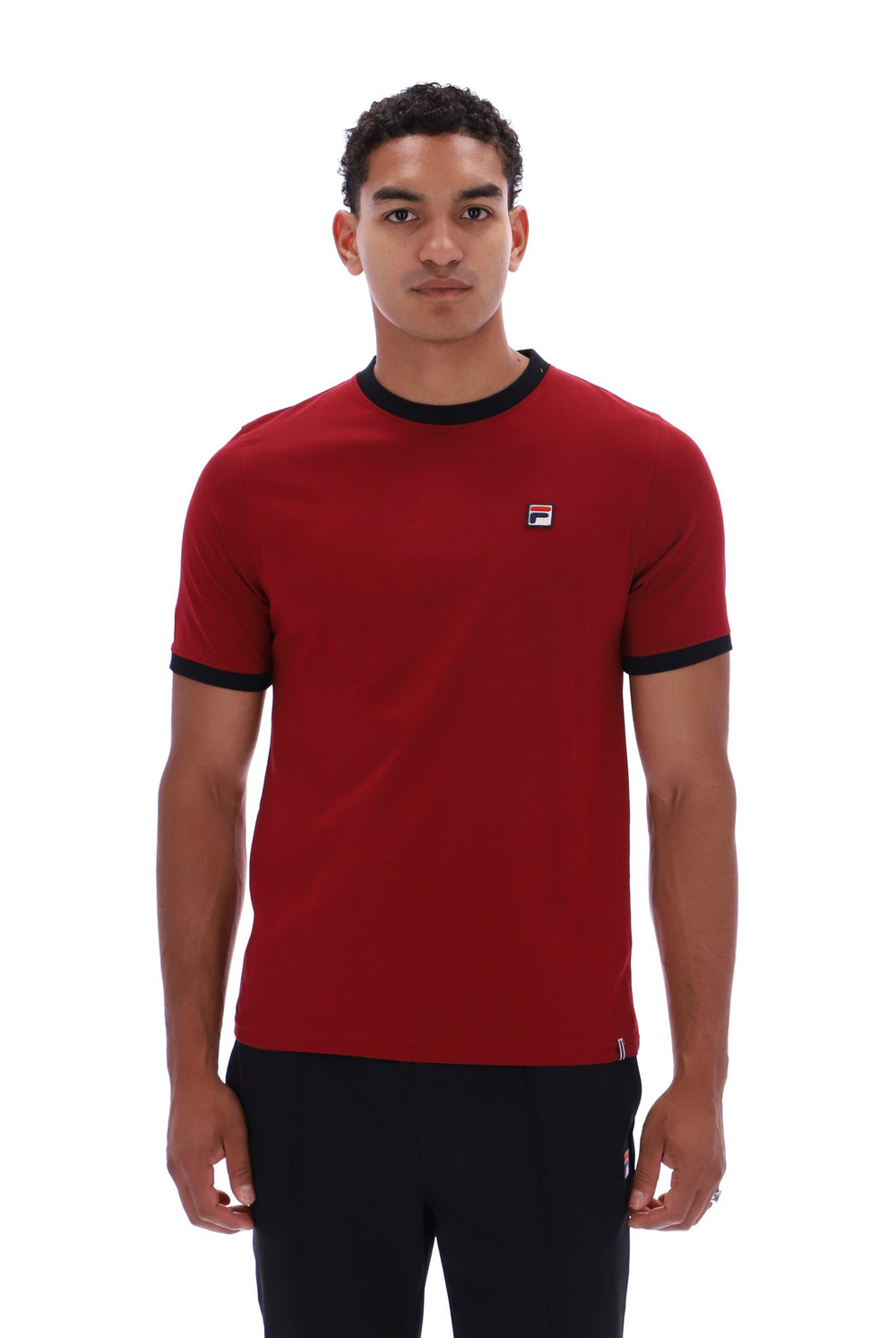 A man wearing a red short-sleeve ringer t-shirt with black trim on the collar and sleeve cuffs, featuring a small white and red Fila logo on the left chest, set against a plain white background.