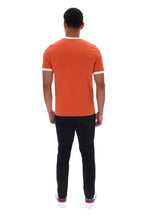 A man viewed from behind wearing a bright orange short-sleeve t-shirt with white trim on the collar and sleeve cuffs, paired with black pants and white sneakers, against a plain white background.
