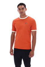 A man wearing a bright orange ringer t-shirt with white trim on the crew neck and sleeve cuffs, paired with black pants, photographed against a solid white background.