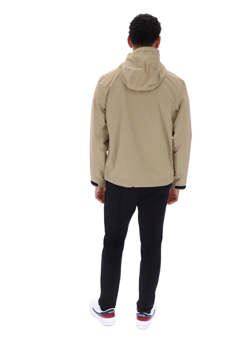 A man viewed from behind wearing a beige hooded jacket, black pants, and white sneakers with red accents, set against a plain white background.