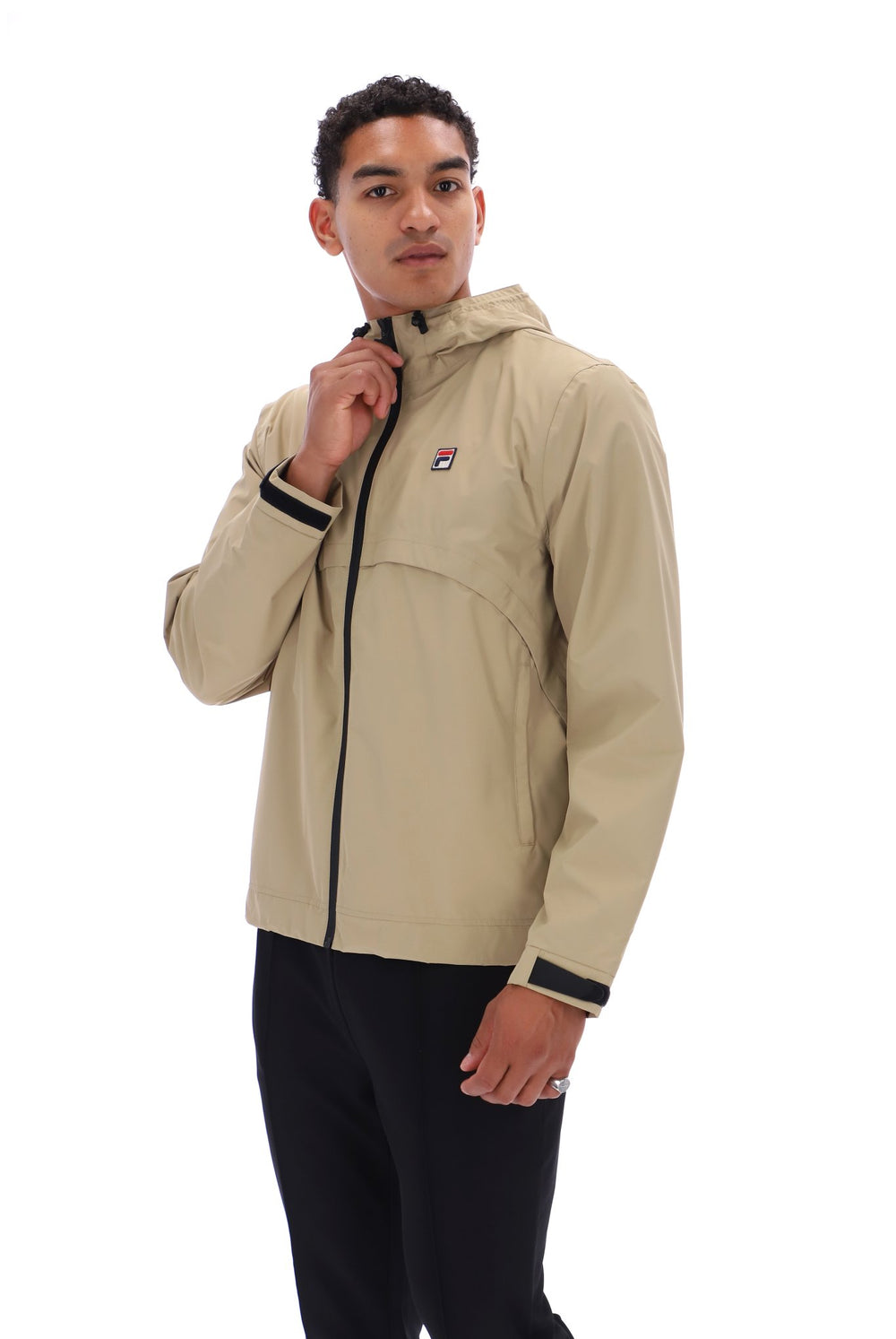 A man wearing a beige hooded jacket with black trim and a small red, white, and blue logo on the chest, paired with black pants, photographed against a plain white background.