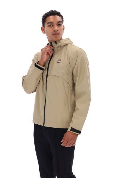 A man wearing a beige hooded jacket with black trim and a small red, white, and blue logo on the chest, paired with black pants, photographed against a plain white background.