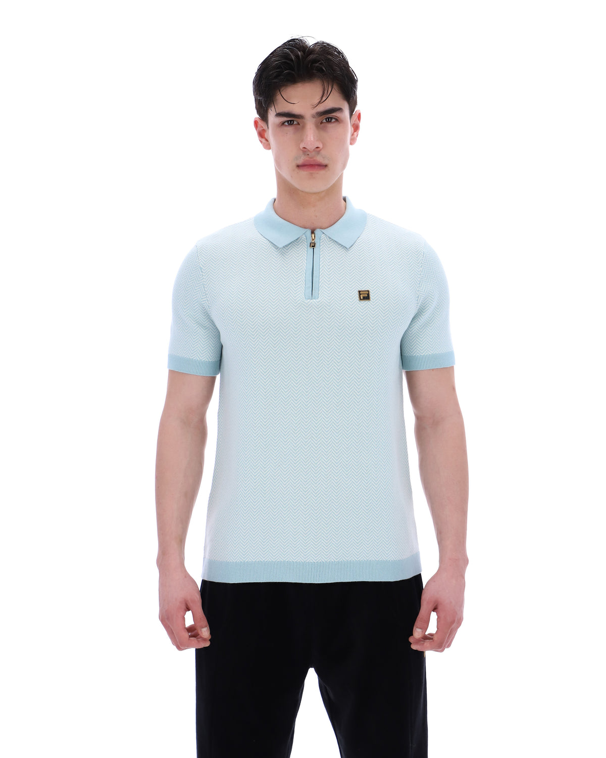 Man wearing a light blue polo shirt with a small logo on a white background