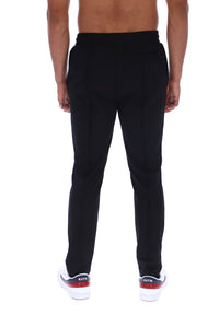 Rear view of a man wearing black slim-fit sweatpants and white sneakers with red and blue accents, against a plain white background.