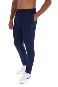 A man wearing navy blue sweatpants with a small Fila logo on the left thigh, paired with white sneakers, shown from the waist down on a white background.
