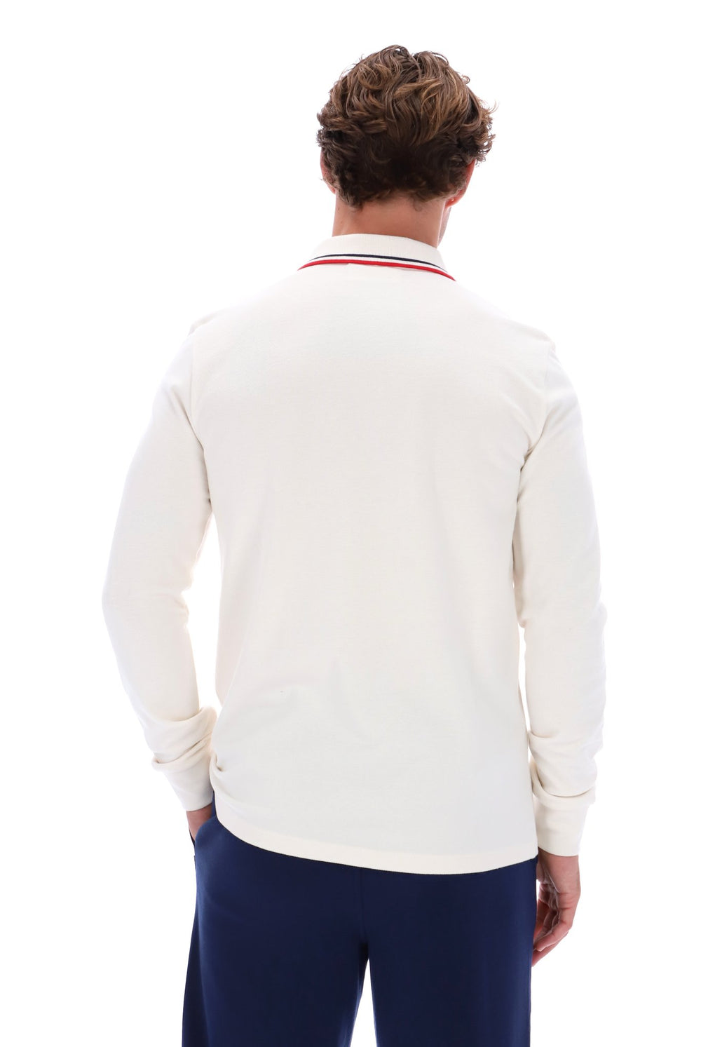 A man viewed from behind wearing a cream long-sleeve polo shirt with a red and blue striped collar, paired with navy trousers, against a solid white background.