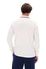 A man viewed from behind wearing a cream long-sleeve polo shirt with a red and blue striped collar, paired with navy trousers, against a solid white background.