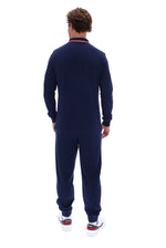 A man viewed from the back wearing a navy blue long-sleeve tracksuit with a red and white striped collar, paired with white sneakers.